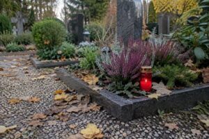 Rotes Grablicht auf einem Grab mit Heidekraut im Herbstlicht, Laub auf dem Friedhofsweg